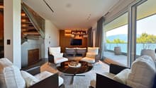 Modern living room with large windows, white chairs, black marble coffee table, and a TV on a wooden shelf.