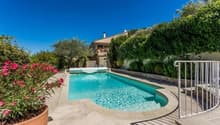 Swimming pool, stone wall, metal railing, plants, flowers, house in the background