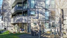 Modern apartment building, concrete exterior, glass windows, balconies on multiple floors, greenery around
