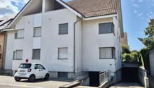 Apartment building with garage, white exterior, red tile roof, solar panels, small car parked in front