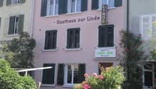 pink building, green shutters, outdoor seating, sign reading Gasthaus zur Linde, flowers, gate