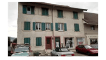 Apartment building, three stories, beige walls, green shutters, several parked cars in front