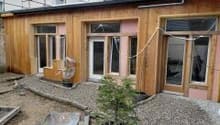 Wooden exterior, pink painted wall, 3 windows, balcony on top floor, gravel driveway, partially completed