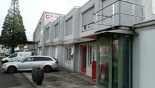 Commercial building with multiple windows, red door, green door, balcony, cars parked in front