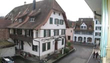 Two story building, brown roof, green shutters, small balcony, parked car