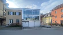 3 story house with a glass facade, garage doors, and an air conditioning unit in the middle, paved parking area in front