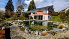 Modern house with swimming pool, brick and white walls, solar panels on the roof, surrounded by a garden with rocks and plants