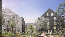 The image shows a residential complex with several multi-story wooden buildings surrounded by a lush, landscaped outdoor area. The buildings have balconies and large windows, and the outdoor space features trees, flowers, and a play area with logs for chi