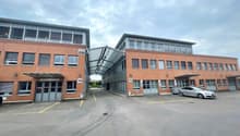 Multi-story commercial building with brick and glass facade, parking spaces in front, numbered entrances