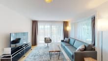 a large living room with windows, couch, sofa, desk, TV, floor lamp, wall lamp