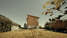 Two-story wooden house with large windows, surrounded by a field of wildflowers and trees. The house appears to be situated in a rural or natural setting with a scenic view.