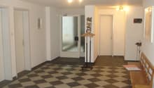 White walls, checkered flooring, wooden bench, glass door, white doors, hanging coat rack, picture frames on wall