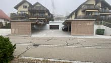Apartment building with carport, driveway, two garages with closed doors, and two covered parking spaces.