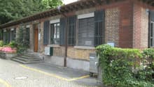 Brick building, black shutters, small garden, brown wooden door, paved walkway