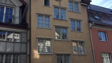 A four story residential building made of bricks, a balcony with an awning, windows with shutters