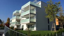 3 story apartment building with balconies, white exterior with glass railings, fenced yard, lawn, and trees