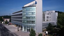 modern office building, glass facade, multiple floors, large parking lot, trees, cars parked