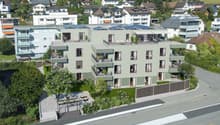 A modern apartment building with multiple floors, solar panels on the roof, balconies, and a garden area.