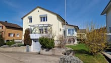 2 story house, yellow exterior, brown roof, garage, balcony, driveway, garden