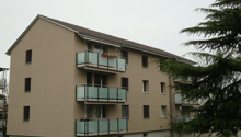3 story apartment building, beige exterior, multiple balconies, green lawn, trees