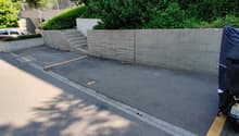 A grey concrete wall with steps, parked car, parking place, a blue cover over an object.