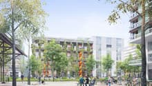 The image shows a modern residential complex with several multi-story buildings surrounded by trees and greenery. The buildings have balconies on the upper floors, and there is a central open space with people sitting at tables and benches, enjoying the o