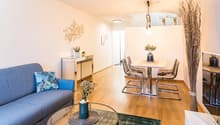 living room with wooden floor, blue couch, glass table, dining table and chairs, plants, wall decorations, lamps