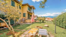 2 story house, yellow, green shutters, large backyard, deck, lounge chairs, trees, fence, mountains in the background