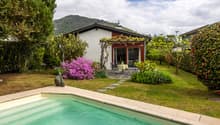 House with swimming pool, garden, patio with table and chairs, red and white exterior, mountain in the background