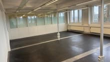 Empty room with white walls, black floor, glass partitions, windows, and overhead lighting.