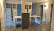Spacious bedroom with built-in closets, a granite-topped island, and a dining table. The room has a modern, minimalist design with neutral colors and tile flooring.