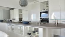 Modern kitchen with stainless steel appliances, granite countertops, white cabinetry, center island, pendant lighting, mirror wall
