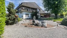 2 story house, gray roof, white walls, balcony, gravel driveway, garden, trees, outdoor seating