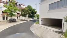 Building facade, visible parking area, garage entrance, streetlight, cars parked on the side.