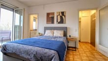 double bed, nightstands, bedside lamps, two paintings on the wall, sliding glass doors to the balcony, wooden floor