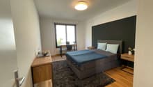 bedroom with bed, desk, chair, radiator, window, rug, lamp, nightstands, flowers