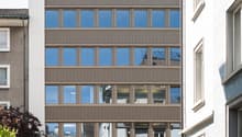 6 story building, glass windows, metal and wood exterior, cars parked at entrance, rooftop terrace