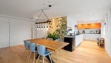 dining table, wooden chairs, kitchen island with cooking area, open shelves, modern pendant light, orange cupboards, wooden flooring