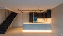 Modern kitchen with open floor plan, sleek black metal staircase, white countertops, integrated sink, and recessed lighting.