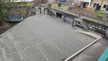 The image shows a raised concrete platform with a grid-like surface, likely serving as a walkway or outdoor area. There are stairs leading up to the platform, and the surrounding area appears to be a residential neighborhood with apartment buildings.