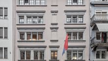A multi-story building with a classical architectural style, featuring arched windows, decorative moldings, and a central pediment. The building has several retail stores on the ground floor, including 'Des petits hauts' and 'Blue Lemon'. A Serbian flag i
