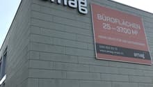 Office building, gray exterior, large sign reading 'amaq', another sign with contact information and services offered