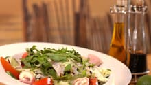 Salad in a white bowl, tomatoes, cucumbers, arugula, ham, cheese.