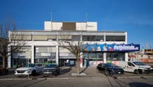 Commercial building with multiple shops, large windows, parking lot in front