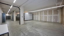 Empty room with concrete floor, white walls, unfinished ceiling, metal shelves, and metal pipes