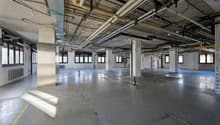 Empty room with concrete floor, metal beams, and visible pipes and wires on the ceiling
