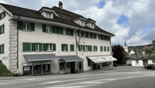 Building with shops on the ground floor, multiple windows with green shutters, chimney, awnings over windows, street sign, parked car