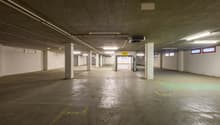 Underground parking lot, concrete floor, white walls, ceiling lights, yellow parking lines, entrance on the right