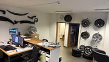 An office with a desk, chairs, computer monitors, a clock, tires, and wheels displayed on the walls.