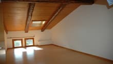 Empty room with wooden floor, wooden ceiling, two windows, and white walls.